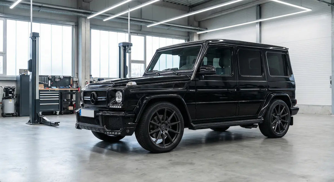 Mercedes-Benz G63 W463a in schwarz, leicht seitlich von vorne fotografiert, steht in einer sauberen, modern beleuchteten Werkstatt mit Hebebühne im Hintergrund.