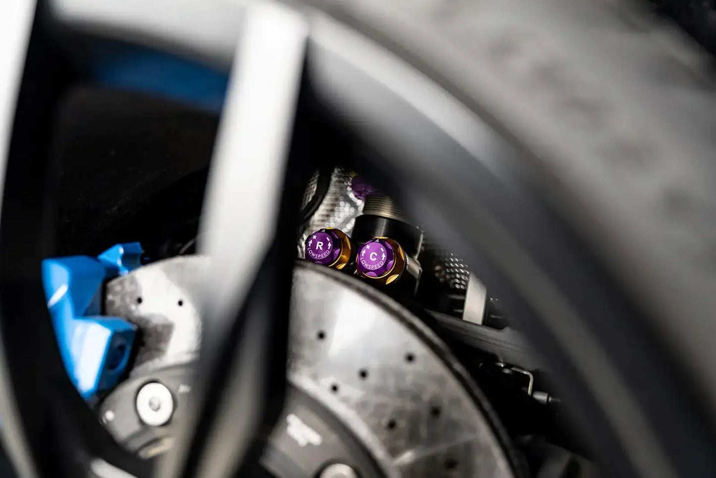 Detailaufnahme Sportwagen-Bremse mit blauem Bremssattel und violett-goldenen Tuning-Teilen